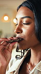 Bite, chocolate and satisfaction with Indian woman in home living room for craving or indulgence. Candy, eating and snack with happy person in apartment for delicious junk food, hunger or sweet treat