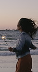 Happy woman, celebration and beach with sparklers for party, new year or festive season in nature. Excited, female person or playing with fireworks, twirl or smile on ocean coast for outdoor freedom