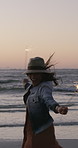 Excited woman, celebration and beach with sparklers for party, new year or festive season in nature. Happy, female person or playing with fireworks, twirl or smile on ocean coast for outdoor freedom
