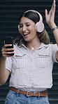 Happy woman, dancing and phone with headphones for music or listening on garage door. Female person, user or smile with songs, sound or mobile smartphone for audio streaming app, energy or vibe