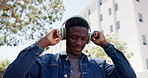 Streaming, dancing and black man in city with headphones, energy and freedom on outdoor walk. Audio, movement and male person in town with technology, rhythm or enjoyment with music subscription.