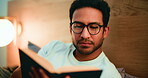 Late, man and reading book in bedroom with glasses for entertainment, cozy activity or literature. Night, person and comfortable with eyewear in apartment for fiction story, novel and relaxing hobby.