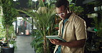 Man, florist and typing with tablet at store, inventory management or contact supplier for stock. African person, tech and botanist with notes, application and checklist for order at flower shop