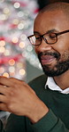 Black man, reading and phone at house on Christmas for social media, browsing web and gift search. Smile, male person and mobile app for online shopping, funny meme and festive celebration with bokeh