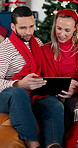 Christmas, tablet and happy couple relax in home, gift shopping and decision for sale on sofa. Xmas, man and woman with technology in living room for festive purchase, talking and point on holiday