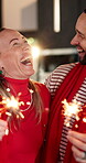 Christmas, couple and laugh with sparklers in home for celebration, festive season and bonding. Hug, people and funny with fireworks in house for holiday tradition, December fun and love relationship