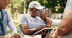 Tablet, food drive and senior volunteers in nature for charity, non profit and community outreach. Digital technology, packing and group of ngo employees with groceries distribution outdoor in park.