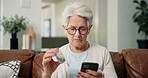 Senior woman, phone and sofa with medication for telehealth, research or symptoms in home. Elderly, female person or patient scrolling with mobile smartphone or pills for online side effects in house