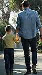 Father, child and holding hands in street with walk, protection and connection for bonding together. Back, dad and happy son stroll in neighborhood with security, support and outdoor for fresh air.