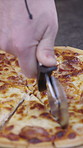 Person, hands or cutting with pizza for meal prep, italian recipe or catering service above in home. Top view, closeup or pastry chef slicing with cheese for food serving, dining or cuisine on table 