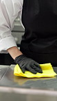 Wiping counter, person and chef in kitchen, cleaning and detergent with routine. Closeup, spray bottle and employee with cloth, hygiene and remove bacteria for safety, workstation and sanitation