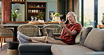 Senior woman, phone call and laptop on sofa, smile or holiday planning in living room at house. Elderly person, happy and talk with tech, computer or contact for travel, booking or vacation in home