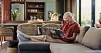 Senior woman, tablet and laptop on sofa, smile or holiday planning in living room at house. Elderly person, happy and scroll with tech, computer or application for travel, booking or vacation in home