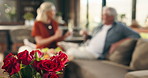 Bouquet, red roses and gift in home for valentines day, toast champagne and celebration for anniversary. Senior couple, drinks and flowers with relationship goals, milestone or relax on sofa in house