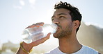 Fitness, outdoor and happy man drinking water with bottle,  restore lost body fluid and hydration. Thirsty, low angle or person with mineral liquid for electrolytes balance, nature and exercise break
