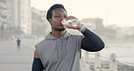 Black man, fitness or drinking with water at beach for workout break, hydration or recovery. Active, male person or runner with mineral liquid, bottle or aqua beverage for sustainability on promenade