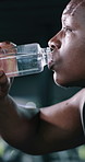 Drinking water, fitness and tired with black man in gym for workout recovery, hydration minerals and detox. Exercise fatigue, electrolytes drink and beverage with person and bottle in sports center