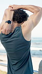 Warm up, fitness and man by beach for running, workout or wellness training on promenade. Sports, boardwalk and back of athlete with arm stretching for cardio exercise by ocean for health in morning.
