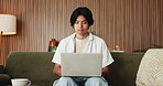 Laptop, remote work and startup with Asian man on sofa in home living room for planning or research. Computer, development and typing with freelance entrepreneur in apartment for small business