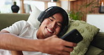 Happy man, headphones and phone on couch in home, chat and audio subscription in living room. Person, smartphone and listen to music on sofa, streaming service or mobile app for social media at house