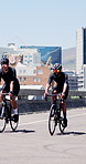 Friends, bicycle and cycling in city with fitness, smile and conversation with training on urban bridge. Men, bike and cardio challenge in street, happy or chat for exercise with sunglasses in town
