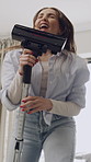Woman, vacuum cleaner and happy for singing in living room for dancing, fun and hygiene in home. Person, smile and playful with appliance for dust, dirt or spring cleaning with voice at apartment