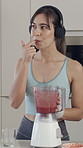 Woman, blender and lick with taste in kitchen with headphones, streaming and nutrition in home. Person, happy and listen to music with smoothie, finger and diet for detox with benefits at apartment