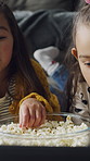 Popcorn, relax and children in home for watching tv, movie or series together on weekend. Bonding, happy and girl kids eating snack for streaming film with online subscription in living room at house