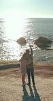 Drone, hug and pointing with couple on beach together for bonding, romance or scenic view at sunset. Aerial, back and ocean with people outdoor on coast for holiday, travel or vacation in summer