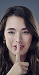 Face, finger and woman with quiet in studio, confidential secret and sensitive information for silence. Portrait, private news and person with hush for unknown announcement, smile and gray background