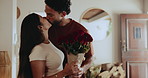 Roses, kiss and couple in home with gift, surprise or bonding on valentines day together. Happy, love and man with red flowers for woman with romantic present for anniversary in living room of house.