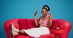 Excited, smartphone and black woman on sofa in studio, relax and message to contact. Celebration, smile and African person on couch, cellphone for social media, app and cheering on blue background