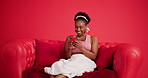 Happy, smartphone and black woman on couch in studio, funny meme and message to contact. Laughing, smile and African person on sofa, cellphone for social media, internet and typing on red background