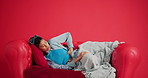 Frustrated, woman and stomach ache on sofa in studio for period cramps on a red background. Female person, model or sore tummy with indigestion, gastrointestinal reflux or menstruation cycle on space