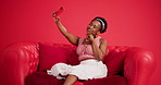 Selfie, smartphone and black woman on sofa in studio, relax and social media to capture moment. Mobile user, smile and African person on couch, cellphone and app for photography on red background
