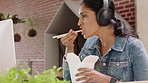 Headphones, businesswoman and eating noodles with computer, streaming audio or review for news story. Chinese food, hungry and person in startup office for music, reading report and creative article