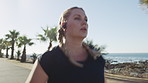 Woman, fitness and running with earphones on sidewalk or promenade for workout or exercise. Active, female person or runner with sprint or race for cardio training, health or wellness by ocean coast