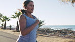 Woman, fitness and running with earphones on promenade or ocean coast for outdoor workout. Active, female person or runner with sprint or exercise for cardio training, health or wellness on sidewalk