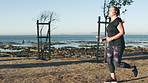 Woman, fitness and running with earphones in nature or ocean coast for outdoor workout. Active, female person or runner with sprint or exercise for cardio training, health or wellness on grass field