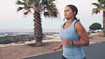 Woman, fitness and running with earphones for exercise or outdoor workout on ocean coast. Active, female person or runner with race or sprint on sidewalk for cardio training, health or wellness