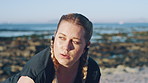 Woman, fitness and break with earphones on beach for workout recovery, intense exercise or training. Active, female person or breathing with sweat, music or sound for outdoor rest, health or wellness