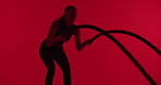 Workout, woman and battle rope in studio for fitness, strength training and cardio on red background. Exercise, strong and person with equipment for muscle development, endurance or power with health