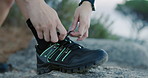 Hands, hiking and tying shoes for exercise on rocks for safety, fitness or summer adventure. Person, legs and hiker with boots, feet and outdoor with laces, trekking and rest on ground in nature