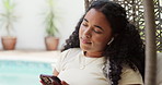Earphones, relax and woman on hanging chair outdoor with texting, social media or chatting on mobile app. Audio tech, music and female person with cellphone for online contact in backyard of home.