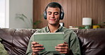 Home, headphones and man on sofa, tablet and listening to music, relax and digital app for song subscription. Hearing, sound and person on couch, tech and streaming for album playlist, radio or audio