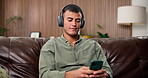Home, smartphone and man on sofa, headphones for sound and listening to music, relax or comfort. Apartment, streaming song or person on couch, rest or digital app for audio, podcast or album playlist