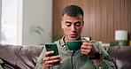 Phone, coffee and man relax in home, reading ebook or morning news with beverage in living room. Tea cup, mobile and happy person on sofa for entertainment, check forum or online article in house