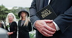 Hands, bible and pastor at cemetery for funeral, service and crowd with Christianity for mourning. People, priest and reverend with family, holy scripture or sermon for burial ceremony at graveyard