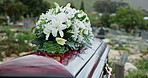 Flowers, casket and funeral at graveyard for burial service, ritual or memorial outdoor for loss. Grief, mourning and coffin with bouquet of floral plants for respect at cemetery for remebrance.