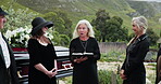 Officiant, family and reading bible for funeral at cemetery, graveyard or outdoor for farewell. Mature, people or group together for grief, death and respect or support for eulogy, book and pastor